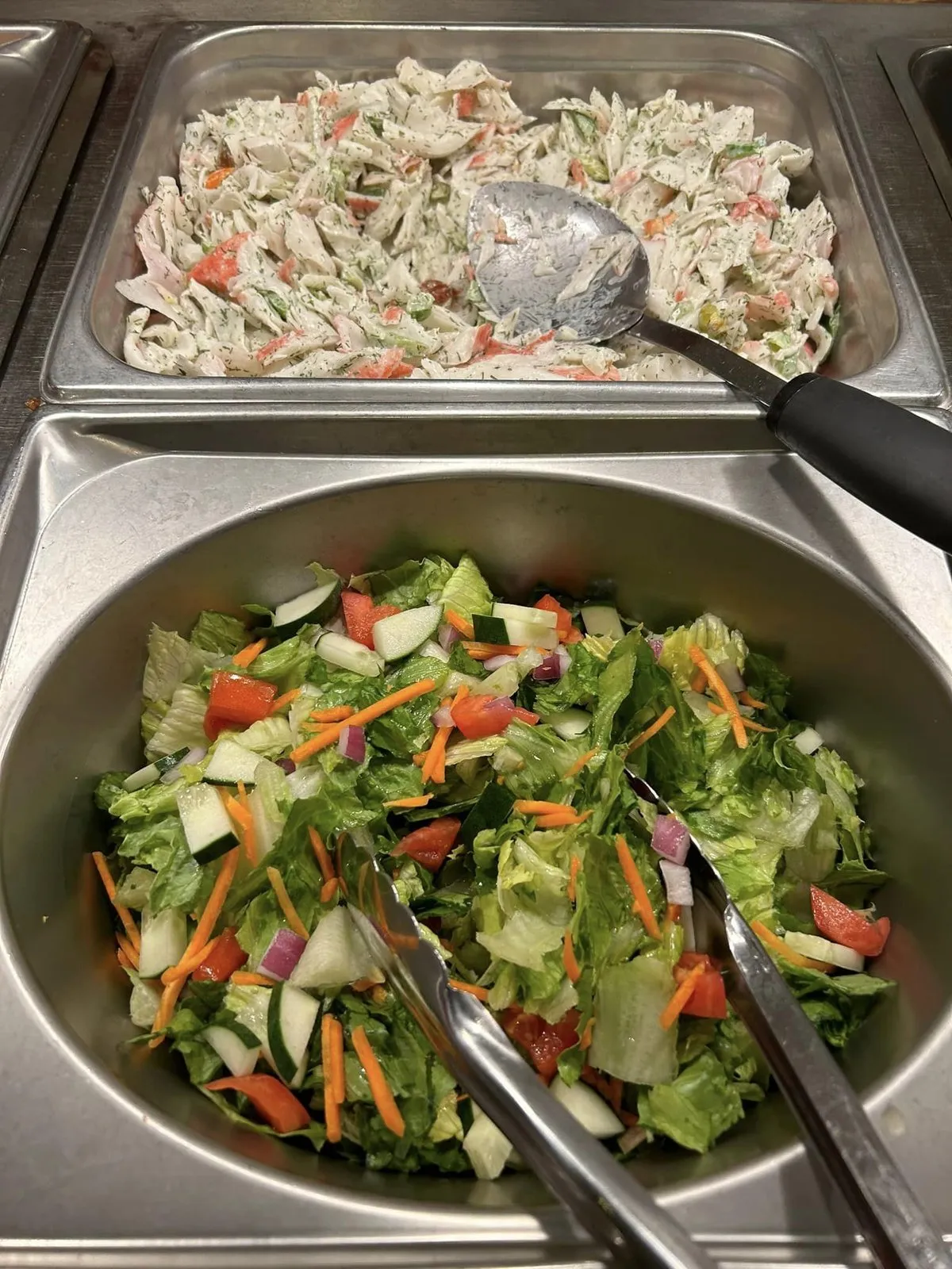Buffet pans of coleslaw and a tossed green salad with carrots, tomatoes and red onion