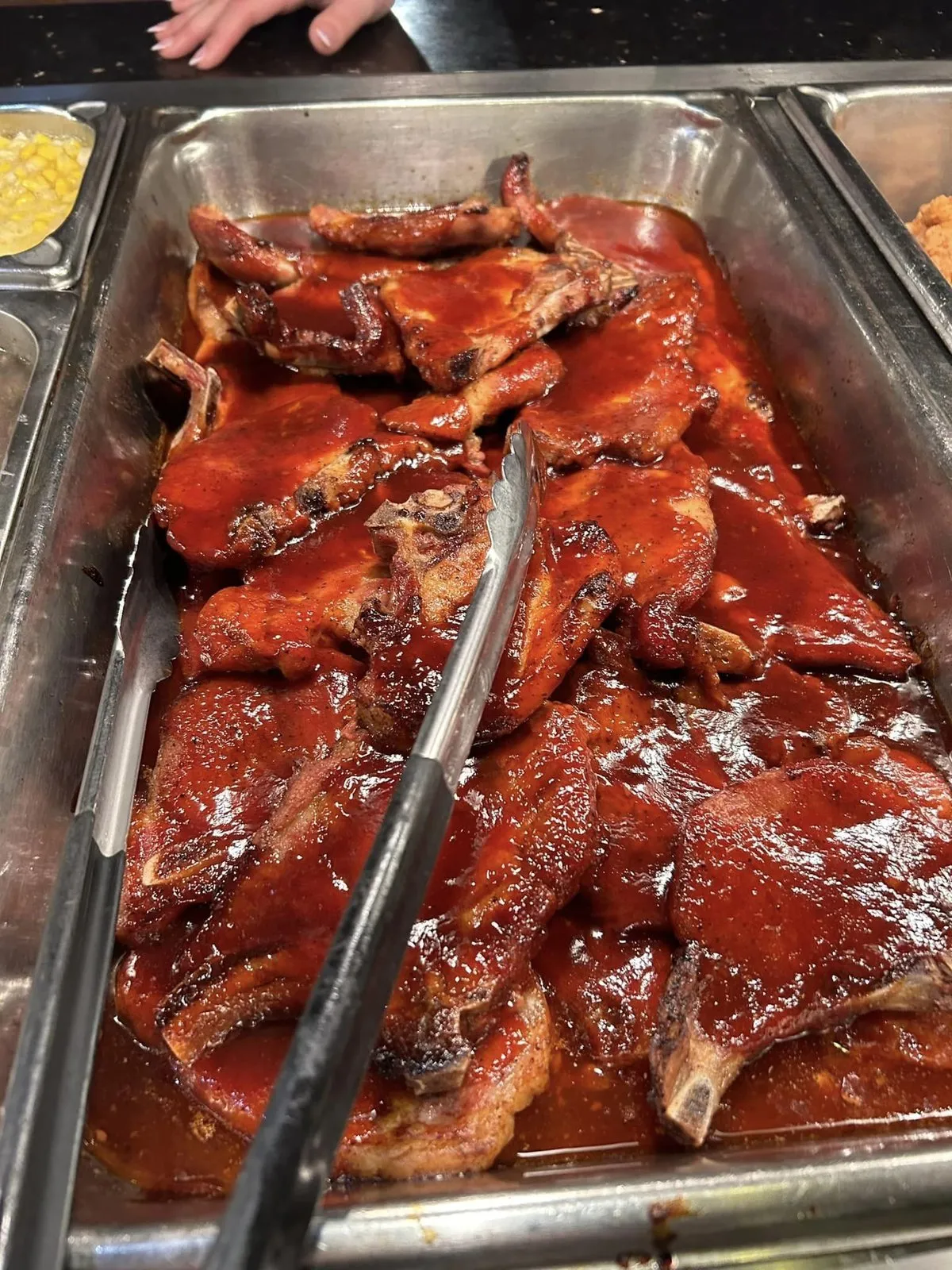 Barbecue-glazed pork chops in a buffet pan with serving tongs